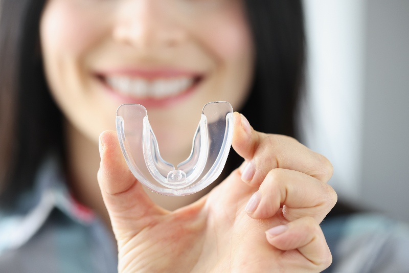 Smiling woman holds transparent plastic mouth guard in her hand